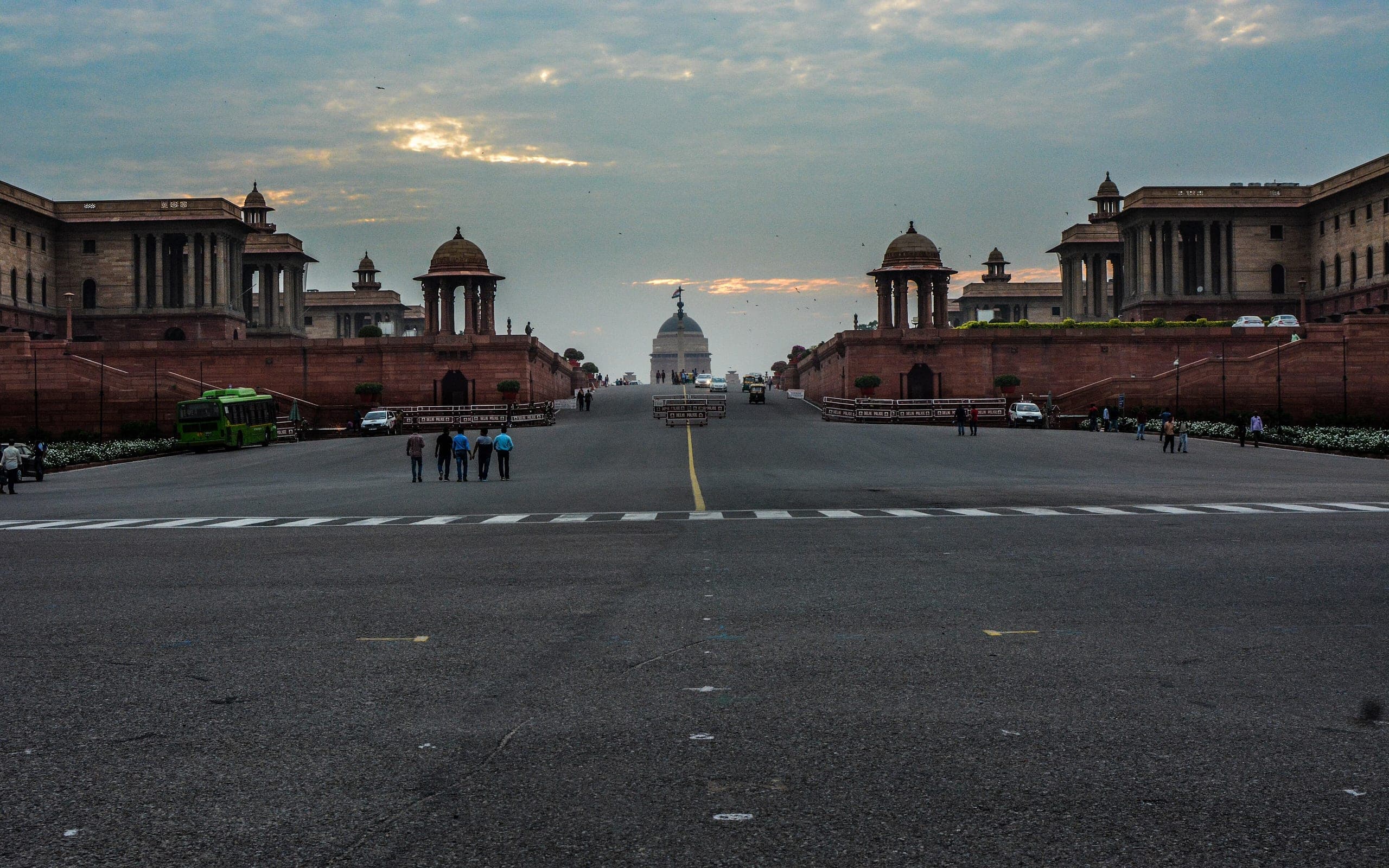 Raisina Hill at dusk — the Secretariat blocks flanking the ceremonial avenue, with the dome of Rashtrapati Bhavan on the axis and a city bus at the kerb.