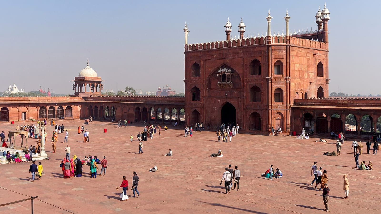 The vast red sandstone courtyard of the Jama Masjid, crowded with visitors, the eastern gateway rising at the right.